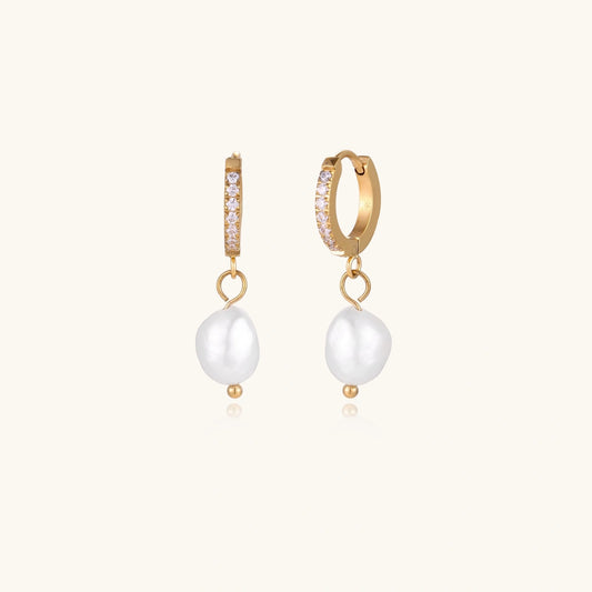 Gold huggie hoop earrings with pavé crystals and white freshwater pearl drops on cream background