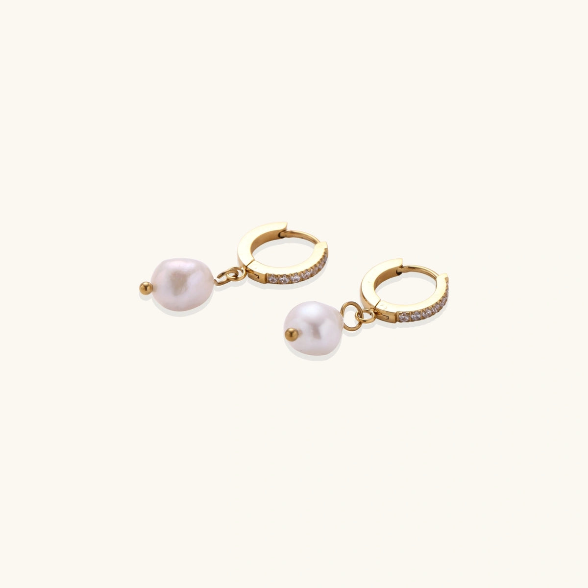 Gold huggie hoop earrings with pavé crystals and white freshwater pearl drops on cream background