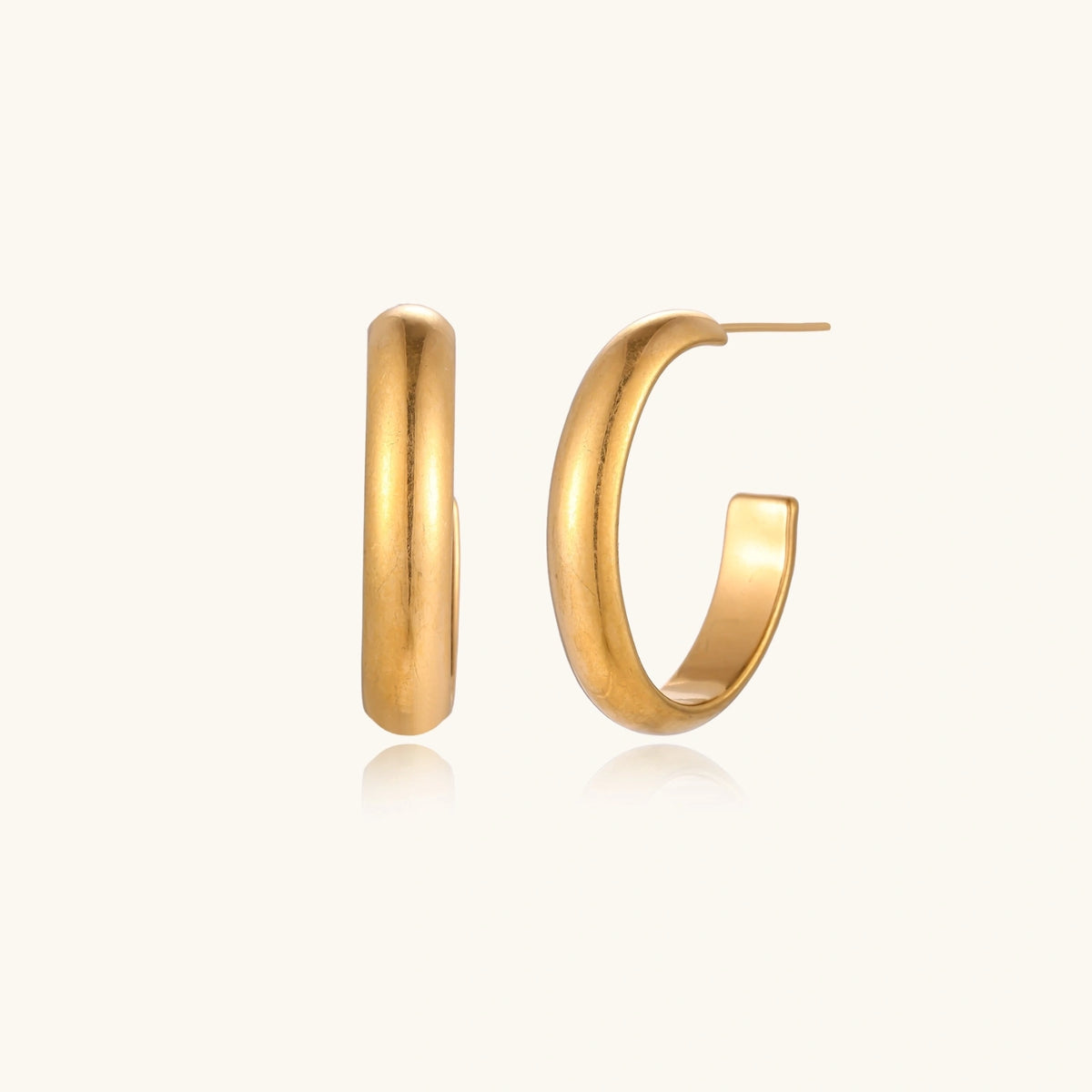 Chunky tubular hoop earrings in warm 14K gold-plated finish with smooth polished surface on cream background.