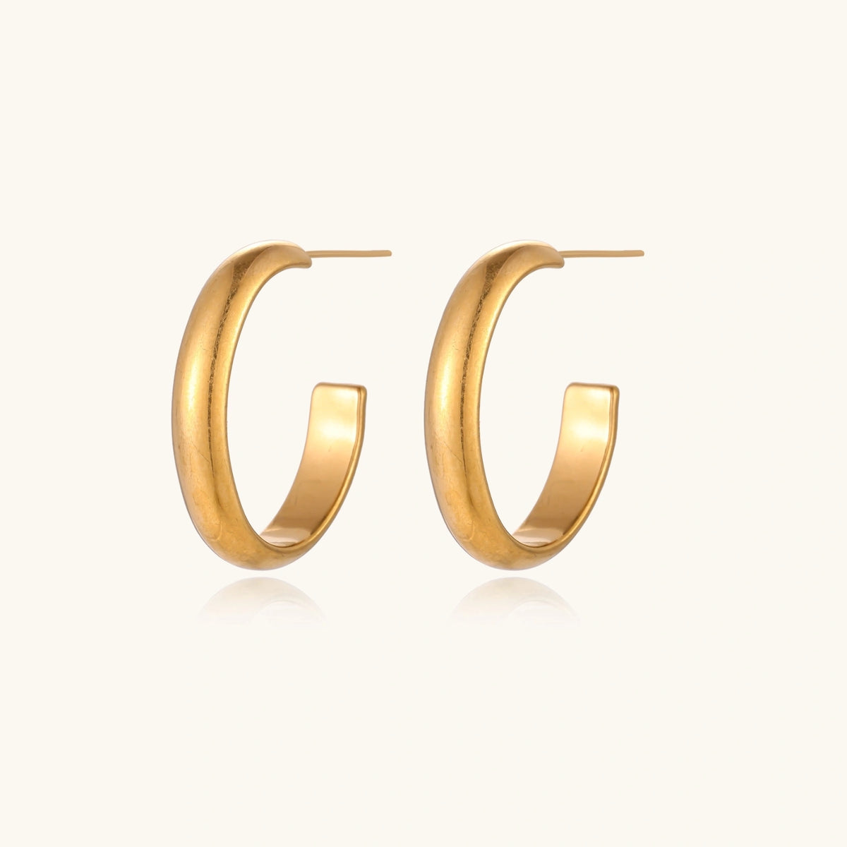 Chunky tubular hoop earrings in warm 14K gold-plated finish with smooth polished surface on cream background.